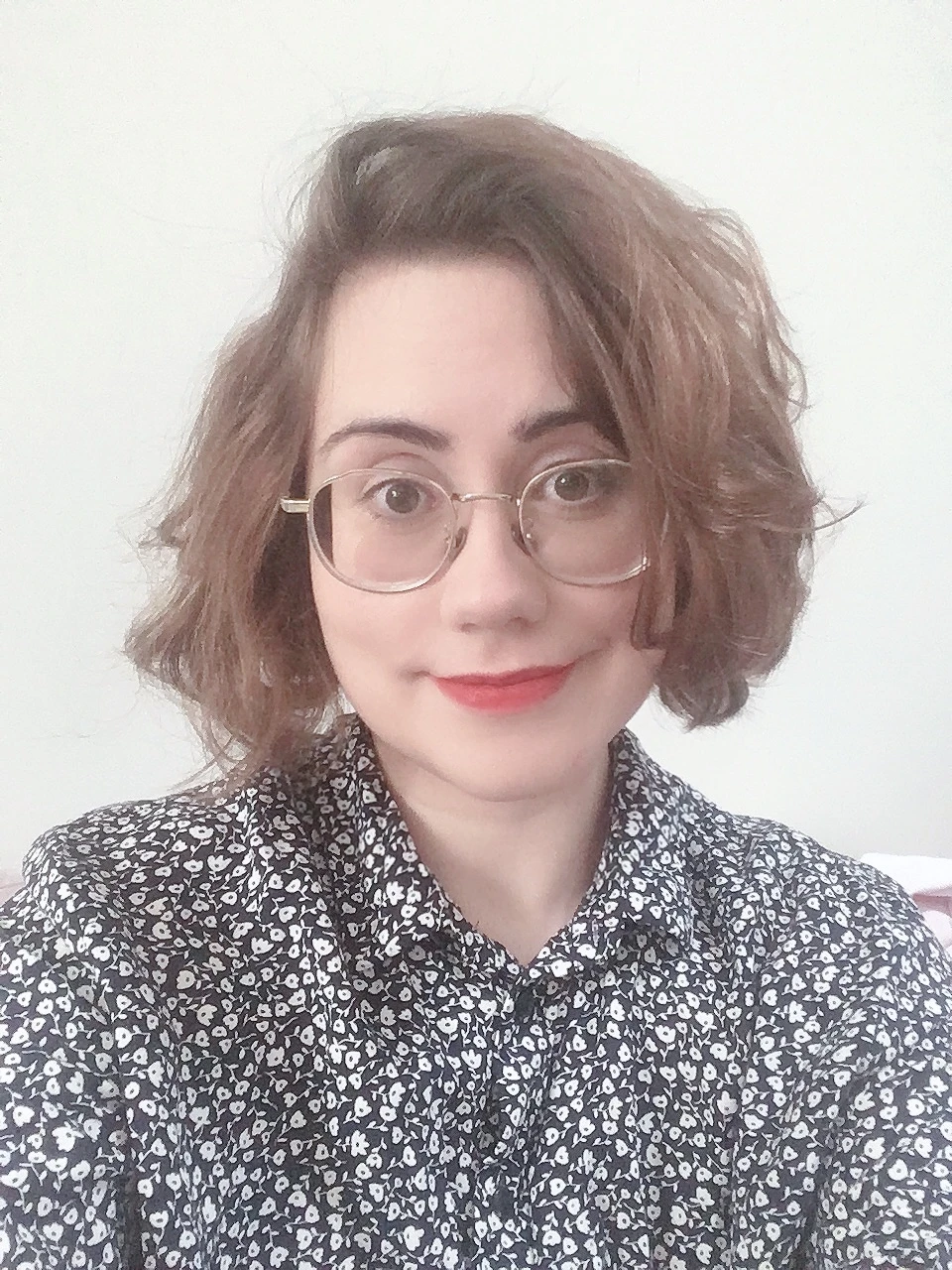 Photo of Emma Winston, a woman with dark hair and glasses wearing a floral shirt and smiling at the camera